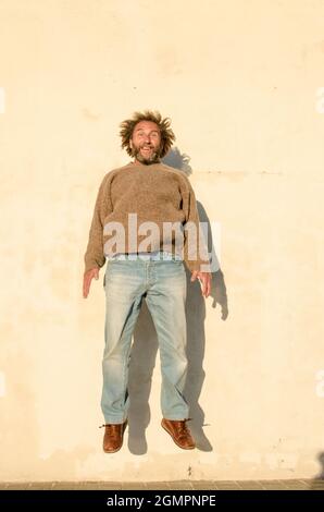 l'uomo di mezza età salta in posizione verticale davanti a un muro bianco Foto Stock