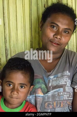 Madre e figlio appoggiati contro un muro di bambù dipinto di giallo nel villaggio di Oinlasi, Timor Ovest, Indonesia. Foto Stock