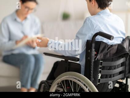 Adolescente handicappato in sedia a rotelle avendo consultato lo psicologo in ufficio, spazio libero Foto Stock