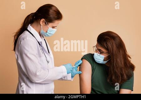 Medico femminile in guanti medici e maschera di vaccinazione paziente Foto Stock