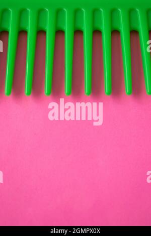 Primo piano di un pettine di plastica verde su una superficie rosa Foto Stock
