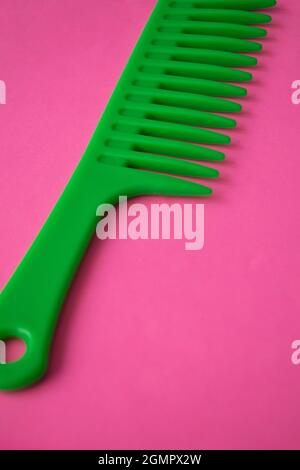 Primo piano di un pettine di plastica verde su una superficie rosa Foto Stock