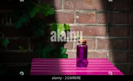Immagine di una bottiglia di vetro con liquido rosa su una superficie rosa al sole Foto Stock