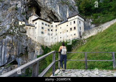 castello predjama costruito in una montagna nella natura vicino alla grotta postojna con una donna turistica che lo guarda . Foto Stock