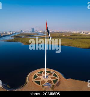 Bandiera nazionale degli Emirati Arabi Uniti e Ras al Khaimah emirano Il punto di riferimento e lo skyline aereo degli Emirati Arabi Uniti del nord vista sopra le mangrovie an Foto Stock