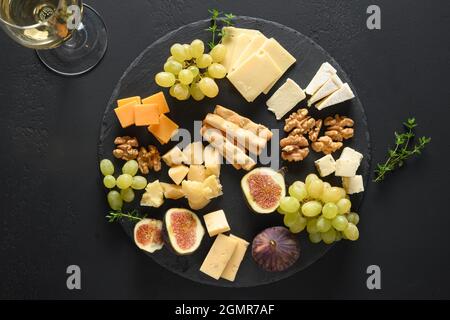 Piatto di formaggi con uva, noci, fichi su sfondo nero ardesia. Vista dall'alto. Spuntino gourmet festivo. Foto Stock