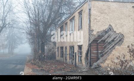 Una casa in legno abbandonata a due piani sulla strada in una giornata di nebbia Foto Stock