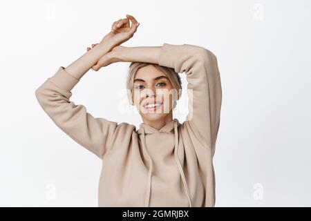 Bellezza. Giovane donna felice alzando le mani e sorridendo spensierato, in piedi rilassato su sfondo bianco Foto Stock