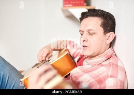 Giovane che suona la chitarra a casa. Concetti di musica, hobby e tempo libero. Messa a fuoco selettiva nella mano destra. Foto Stock