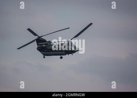 Elicottero CH-47 a rotore tandem RAF Chinook che vola veloce e basso in un cielo grigio blu nuvoloso in un esercizio di battaglia militare, Wilts UK Foto Stock