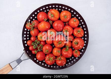 Pomodori ciliegini appena raccolti in una padella per pizze che friggete con buchi per cucinare le verdure per arrostire il cibo a fuoco aperto o carbone. Creativo Foto Stock