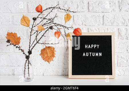 Felice testo autunnale su bordo nero lettera e bouquet creativo di rami con foglie gialle su clothespins in vaso sul tavolo modello per cartolina, gre Foto Stock