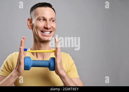 Ritratto di uomo adulto sorridente grins in giallo t-shirt tenendo spazzolino da denti e un mumbell con le mani e guardando da parte Foto Stock