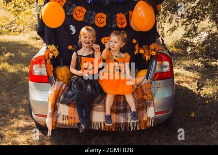 I bambini festeggiano Halloween nel tronco dell'automobile. Amici bambini ragazze che si preparano per la vacanza all'aperto di ottobre. Trick o trunk Foto Stock