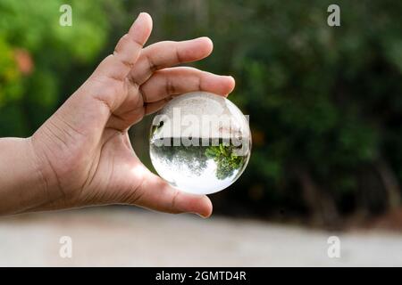 Mano che tiene una sfera di cristallo trasparente con una vista capovolta di un paesaggio. Sfondo sfocato Foto Stock