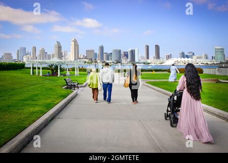 Vista posteriore di una donna con lunghi capelli scuri e di altre persone che si dirigono verso l'area del Coronado Ferry Landing con lo splendido skyline di San Diego, California, in lontananza Foto Stock