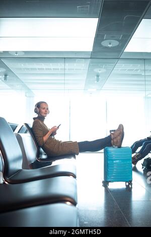 Una donna in attesa dell'orario di imbarco del suo volo al cancello di un aeroporto moderno nell'era pre-covid (immagine a tonalità di colore) Foto Stock