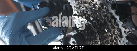 L'handyman con guanti ripara il closeup della cassetta posteriore della bicicletta Foto Stock