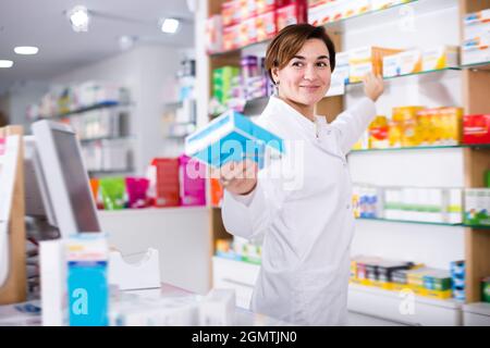 Giovane donna farmacista suggerendo farmaco utile in farmacia Foto Stock