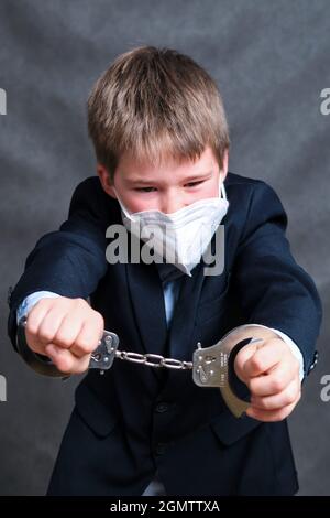 Un ragazzo in una maschera medica sul viso e in manette, copia spazio su uno sfondo nero studio Foto Stock