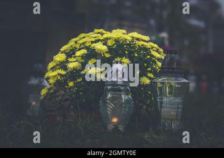 Candele e decorazione floreale da giallo crisantemo fiori su tombe nel cimitero durante il giorno di tutti i Santi Foto Stock