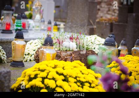 candele ardenti, fiori gialli di crisantemo e decorazioni funebri religiose sulle tombe nel cimitero Foto Stock