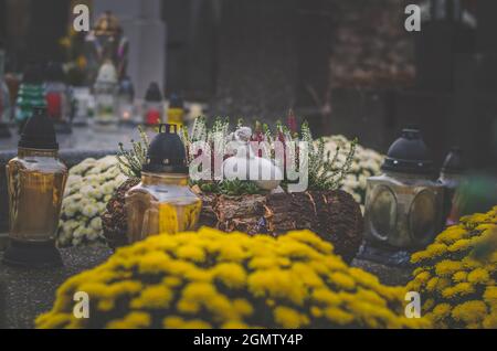 candele ardenti, fiori gialli di crisantemo e decorazioni funebri religiose sulle tombe nel cimitero Foto Stock