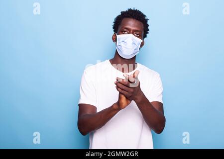 Ritratto di uomo afroamericano che batte e indossa maschera contro l'epidemia di coronavirus. Uomo nero applauding mentre guarda la fotocamera. Afroadulto che usa le mani per applaudire in studio Foto Stock