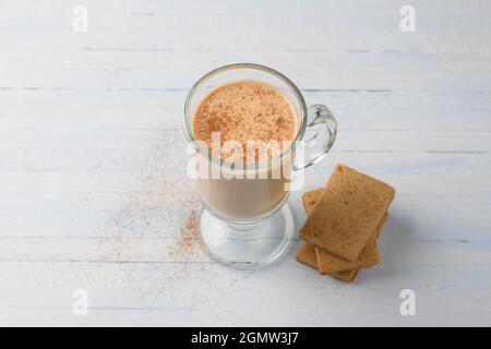 Tè piccante con latte in una tazza di vetro e biscotti di pan di zenzero su sfondo grigio chiaro blu Foto Stock