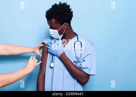 Assistente medico che viene vaccinato dal medico. Medic usando la siringa con l'ago per vaccinare l'infermiere sul braccio per l'assistenza sanitaria e l'immunità. Specialista che riceve un vaccino contro il covid 19 Foto Stock