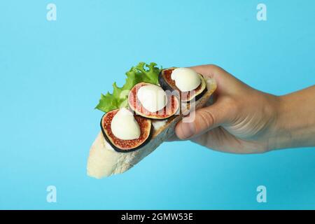 La mano femmina tiene la bruschetta con il fico su sfondo blu Foto Stock