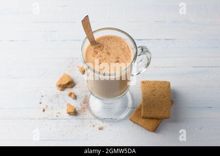 Tè piccante con latte in una tazza di vetro e biscotti di pan di zenzero su sfondo grigio chiaro blu Foto Stock