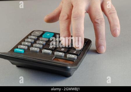 La mano di un uomo conta su una calcolatrice. Un uomo maturo esegue mathè Foto Stock