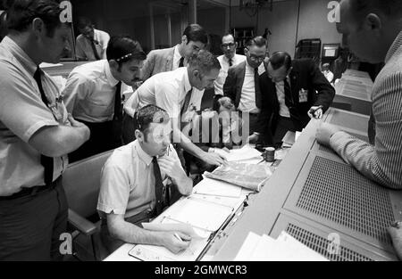 (15 aprile 1970) --- Un gruppo di controllori di volo si riunisce intorno alla console di Glenn S. Lunney (seduto, telecamera più vicina), direttore di volo di turno 4, nella Sala di controllo delle operazioni della Missione (MOCR) del Centro di controllo della Missione (MCC), situato nell'edificio 30 presso il Centro Stecraft (MSC). La loro attenzione è attirata su una mappa meteorologica del sito di sbarco proposto nell'Oceano Pacifico meridionale. Tra coloro che guardano sopra c'è il Dr. Christopher C. Kraft, vice direttore, MSC, in piedi in abito nero, sulla destra. Quando questa foto fu scattata, la missione di atterraggio lunare Apollo 13 era stata cancellata, e il problema-pl Foto Stock