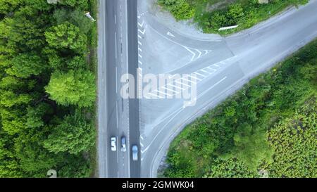 Il movimento di automobili sulla strada asfaltata tra il verde degli alberi, vista aerea dell'intersezione di strade disuguali Foto Stock