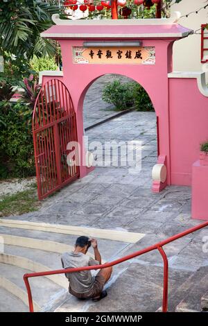 Kuala Lumpur, Malesia - 3 aprile 2011, una persona seduta in vista. Proprio accanto alla linea della monorotaia, questo piccolo e scioccante tempio Daoista rosa richiede t Foto Stock