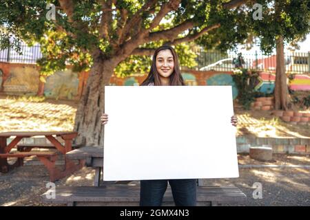 Giovane attivista femminile che mostra una bandiera vuota all'aperto. Ragazza adolescente felice sorridendo alla macchina fotografica mentre tiene un cartello in un parco urbano. Femmina yo Foto Stock