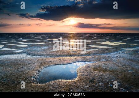 Scatto di una costa di mare spangolata da pietra con l'alba che si riflette sulla sabbia bagnata nei Paesi Bassi Foto Stock