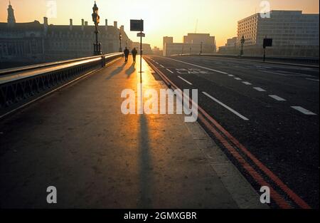 Londra, Inghilterra - 2012; due persone, che si stagliano dal sole nascente, attraversano Westminster Bridge, Londra, all'alba. Foto Stock