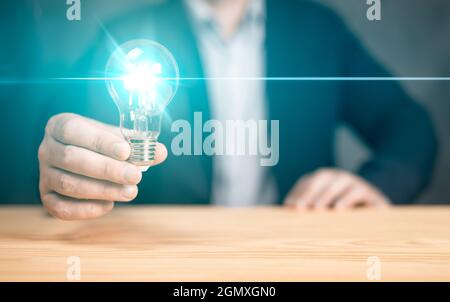 Idea innovativa in mano d'uomo d'affari. Lampada di tenuta manuale su tavola di legno. Concetto di ispirazione pensiero creativo e tecnologia del futuro innova Foto Stock