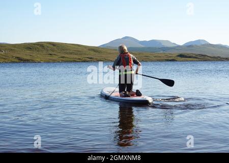 Signora più anziana che usa stand up paddle board Loch Laidon, Highlands scozzesi Foto Stock