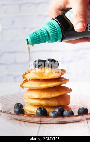 versare lo sciroppo d'acero sulle frittelle con bacche fresche sul piatto Foto Stock