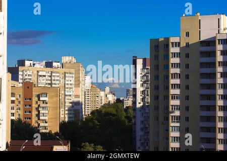 Edifici a più piani contro un cielo blu nelle giornate di sole. Una strada della città, alberi verdi Foto Stock