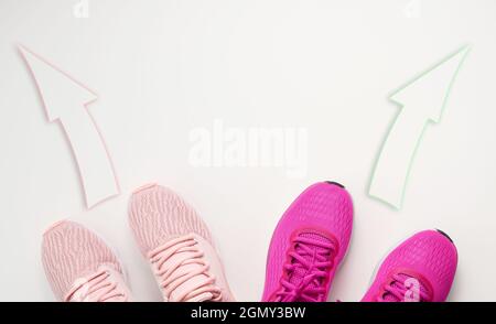 due paia di sneaker rosa in tessuto sono rivolte in direzioni opposte. Concetto di litigio e di divergenza di opinione, percorsi di vita e interessi diversi, Foto Stock