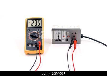 Utilizzando un misuratore digitale, misurare la tensione su una scatola della presa elettrica su sfondo bianco. Foto Stock