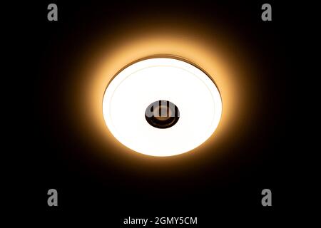 Plafoniera a LED con luce calda e altoparlanti wireless integrati su sfondo nero. Foto Stock