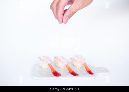 Sushi di gamberi crudi al gamberetto nel ristorante giapponese. Sushi - ama EBI nigiri su tavola bianca su sfondo bianco. Lo chef versa il sale. Foto di alta qualità Foto Stock