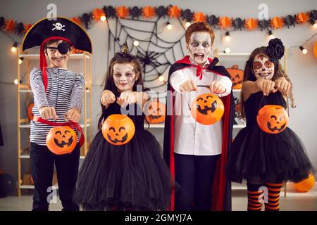 Quattro bambini in costumi di carnevale e con trucco spooky estendono le loro zucche secchi a macchina fotografica. Foto Stock