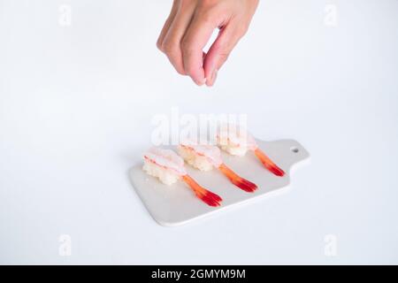 Sushi di gamberi crudi al gamberetto nel ristorante giapponese. Sushi - ama EBI nigiri su tavola bianca su sfondo bianco. Lo chef versa il sale. Foto di alta qualità Foto Stock