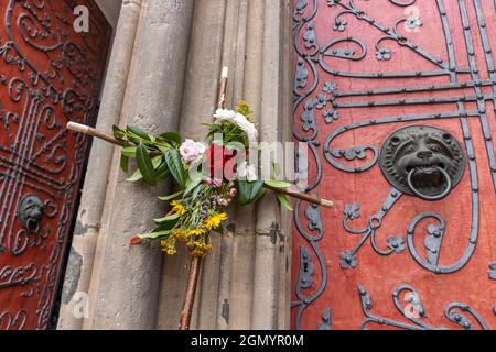 La croce del pellegrino in legno decorata con fiori si affaccia sul portale principale della Chiesa di Santa Elisabetta a Marburg, in Germania, un'importante meta di pellegrinaggio Foto Stock